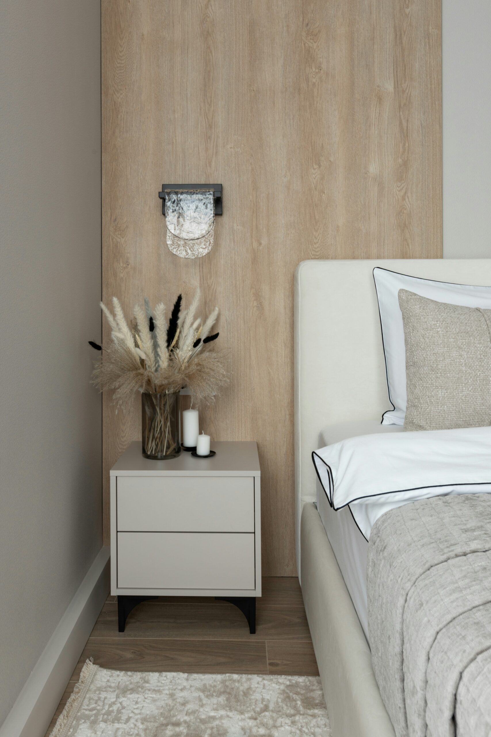 Minimalist nightstand styled with pampas grass, candles, and clean-lined furniture beside a soft upholstered bed.