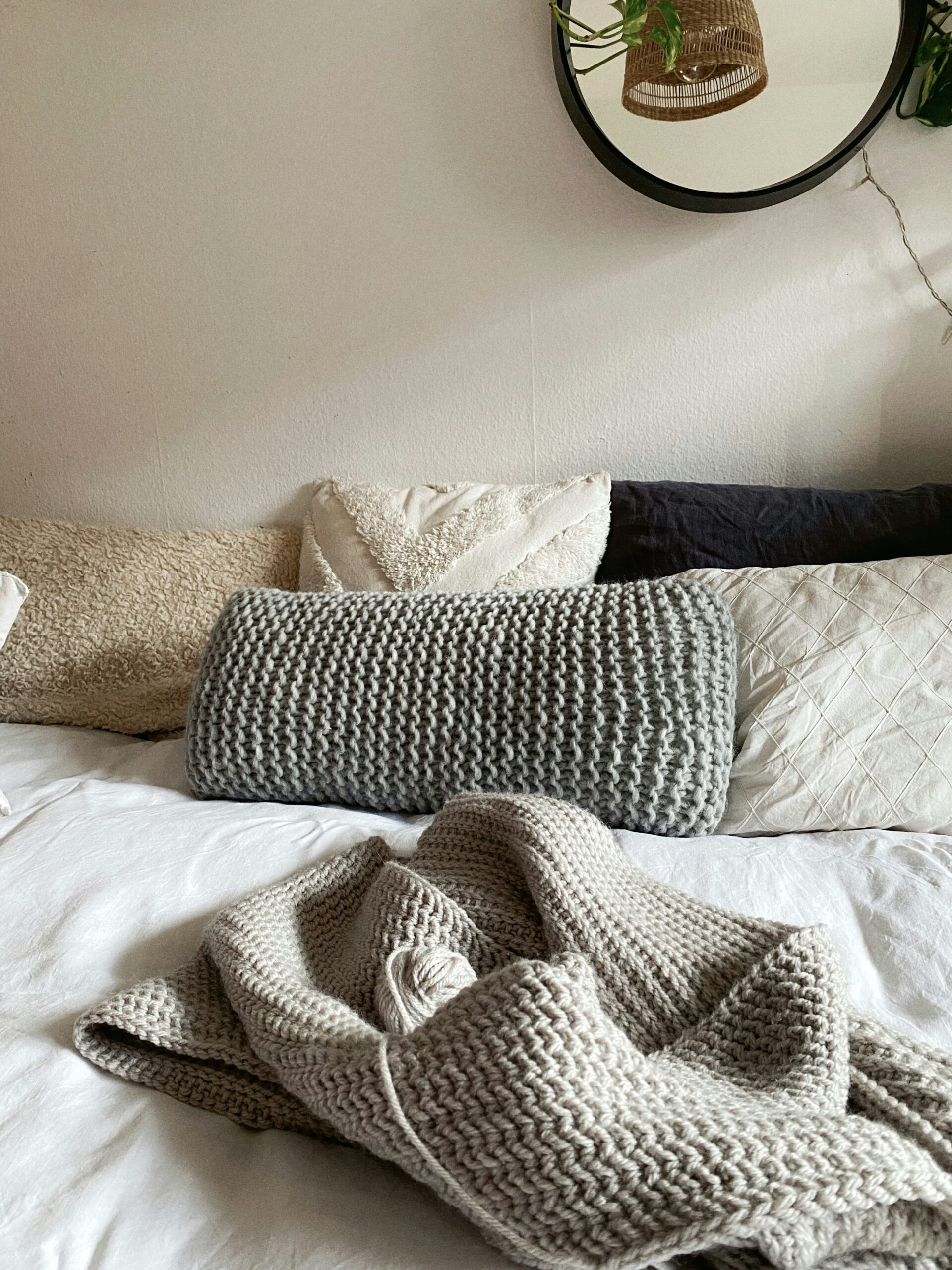 Cozy minimalist bed layered with soft neutral pillows and a textured knit throw blanket.