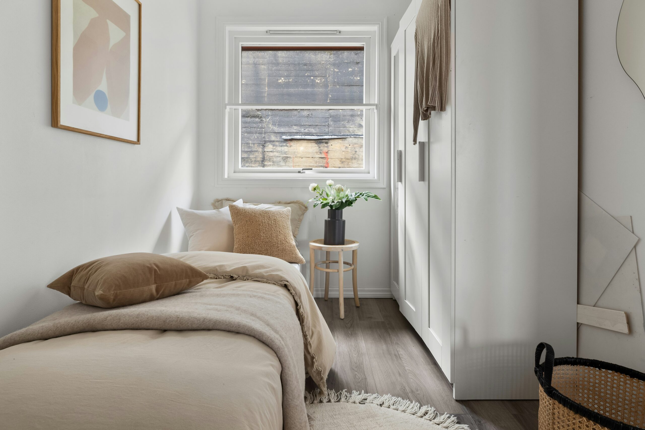 Minimalist bedroom with soft neutral bedding, light wood bed frame, black bedside lamp, and airy white walls.