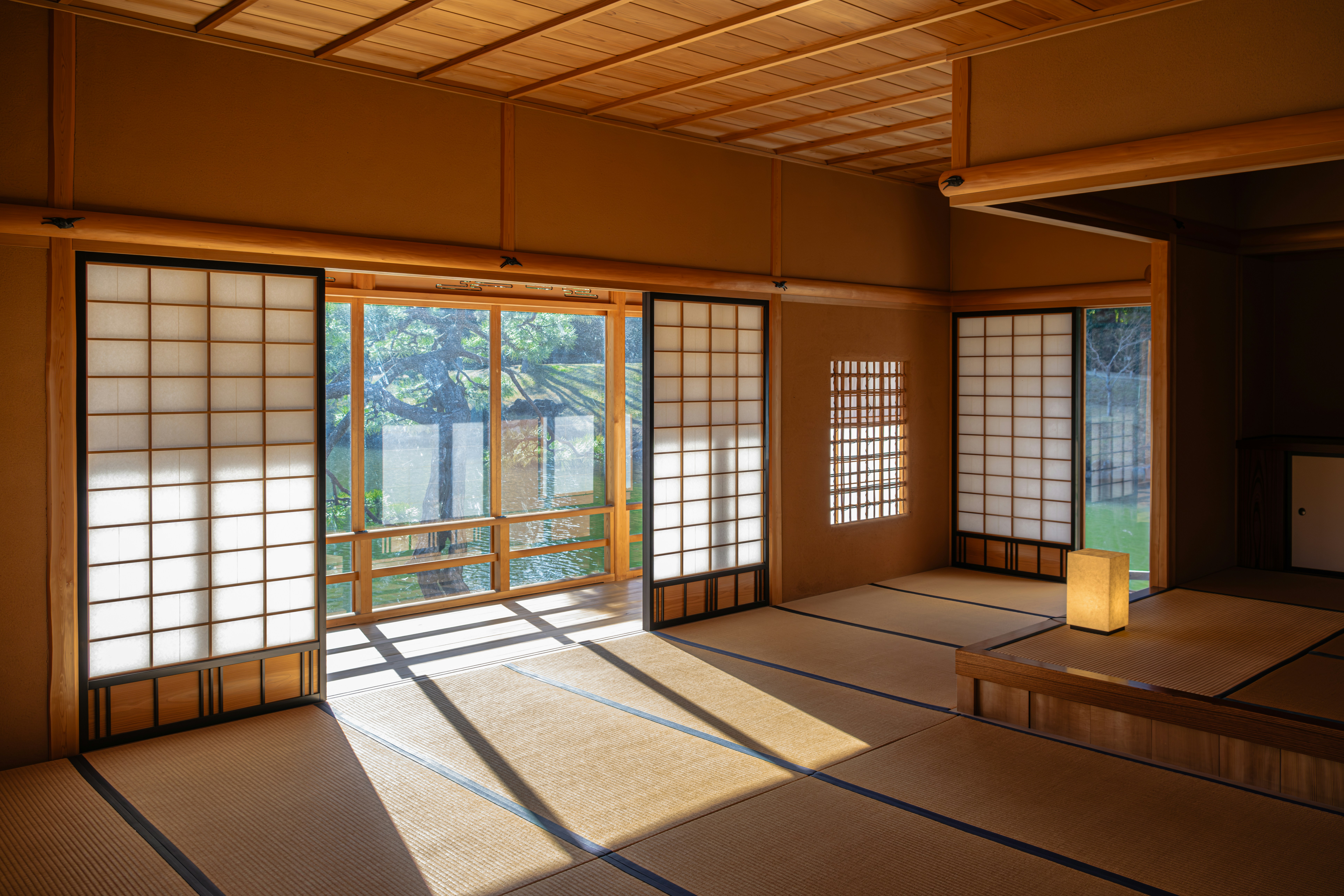 Warm Japandi-style room with tatami flooring, shoji sliding doors, natural wood interior, and soft sunlight creating a calm minimalist living space